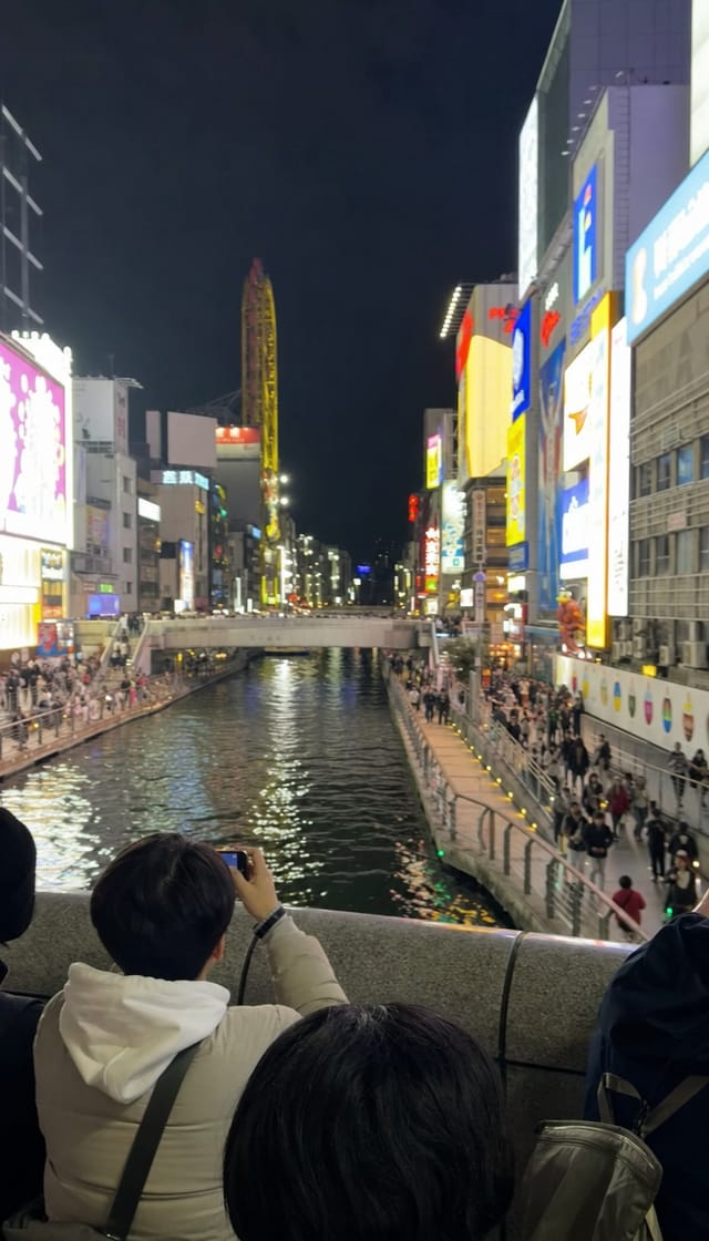 Dotonbori-style canal street at night, huge illuminated signboards, crowds, reflections in the water, phone photo from the bridge